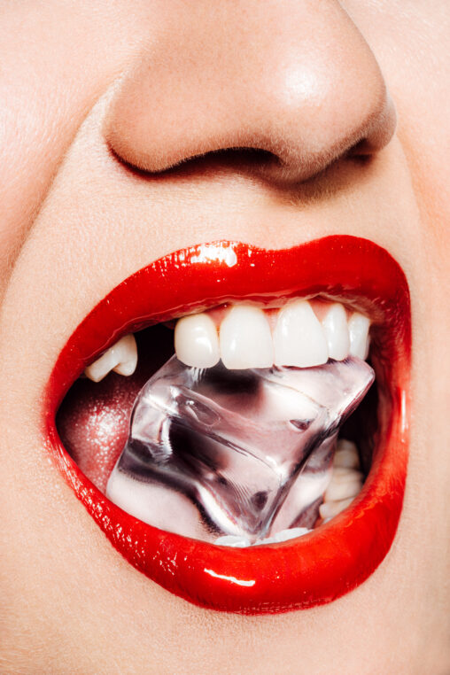 Eine Person hat einen Eiswürfel im Mund und hält ihn zwischen ihren Zähnen.