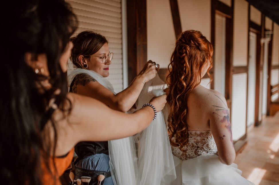 Hochzeitsfoto von einer Braut, die gestylt wird. Ihre Haare werden von zwei Personen gerichtet.